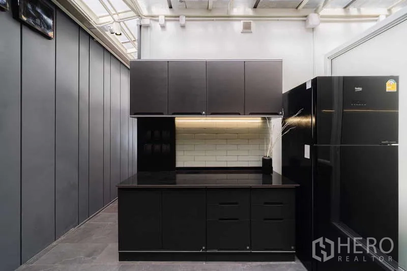 Townhouse for rent or sale in Watthana, Bangkok - Western kitchen view with black island, cabinets, and refrigerator.