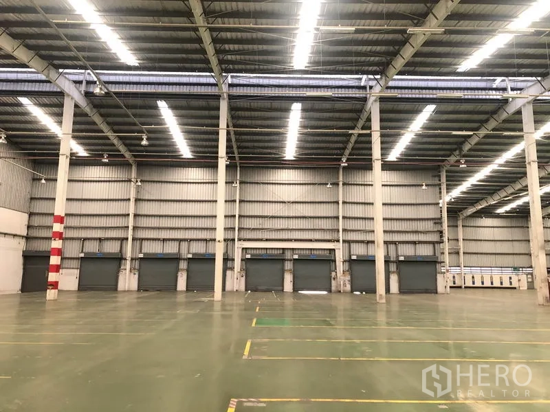 Factory for rent in Phra Nakhon Si Ayutthaya - Interior view toward loading dock doors under bright strip lighting inside the warehouse.