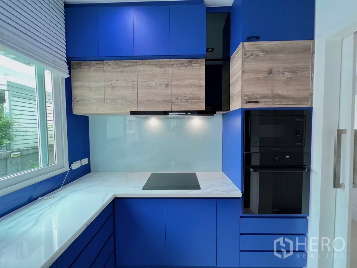 Detached House for rent or sale in Khlong Luang, Pathum Thani - Modern U-shaped kitchen with bold blue cabinetry, induction hob and white counters.