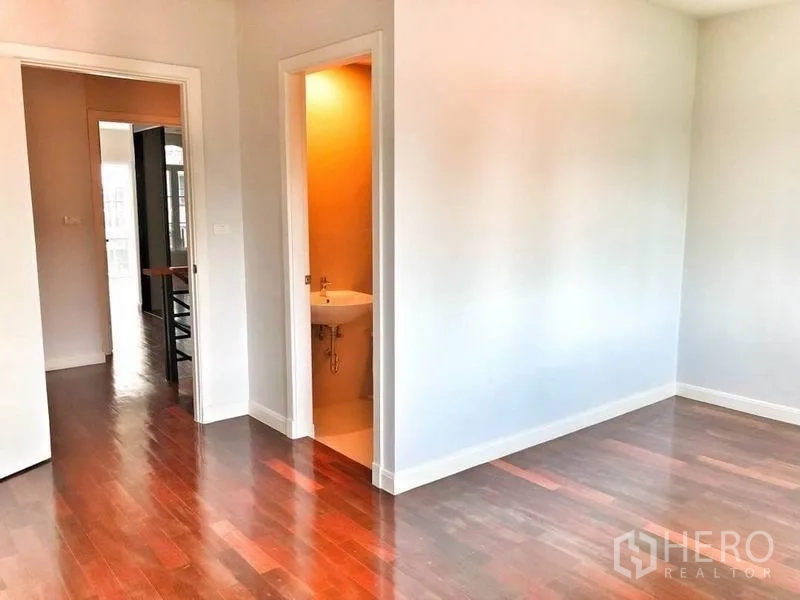 Townhouse for rent in Watthana, Bangkok - Sunlit bedroom corner with doorway to bathroom and hardwood floors.