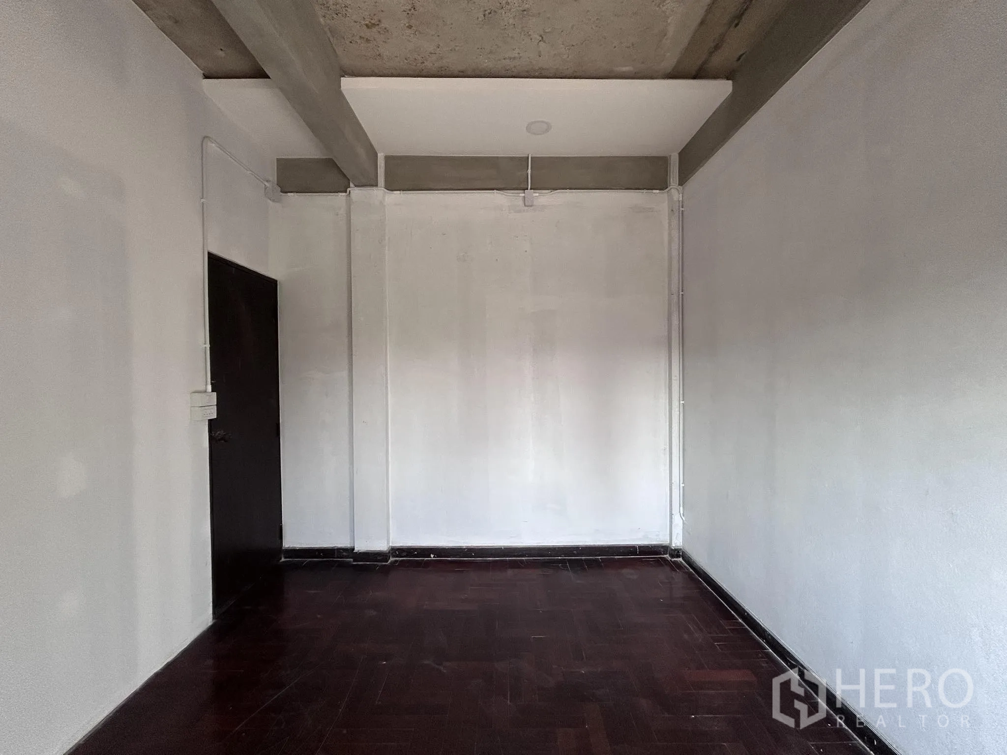 Home Office for rent or sale in Watthana, Bangkok - Empty room with dark wood floor, simple walls and ceiling beams.