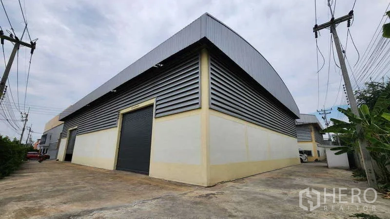Factory for rent in Ban Phaeo, Samut Sakhon - Factory exterior with corrugated metal cladding, large roller shutters and a wide driveway for container trucks.
