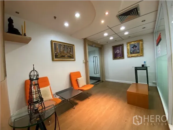 Office Space for rent in Khlong Toei, Bangkok - Cozy reception lounge with orange chairs, small tables, wall art and recessed ceiling lights.