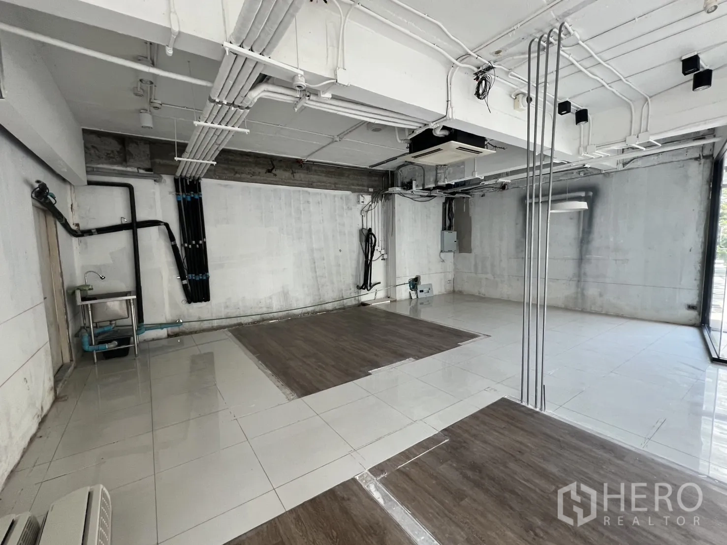 Retail Space for rent - Back service area showing utility pipes, a stainless sink and exposed conduits.