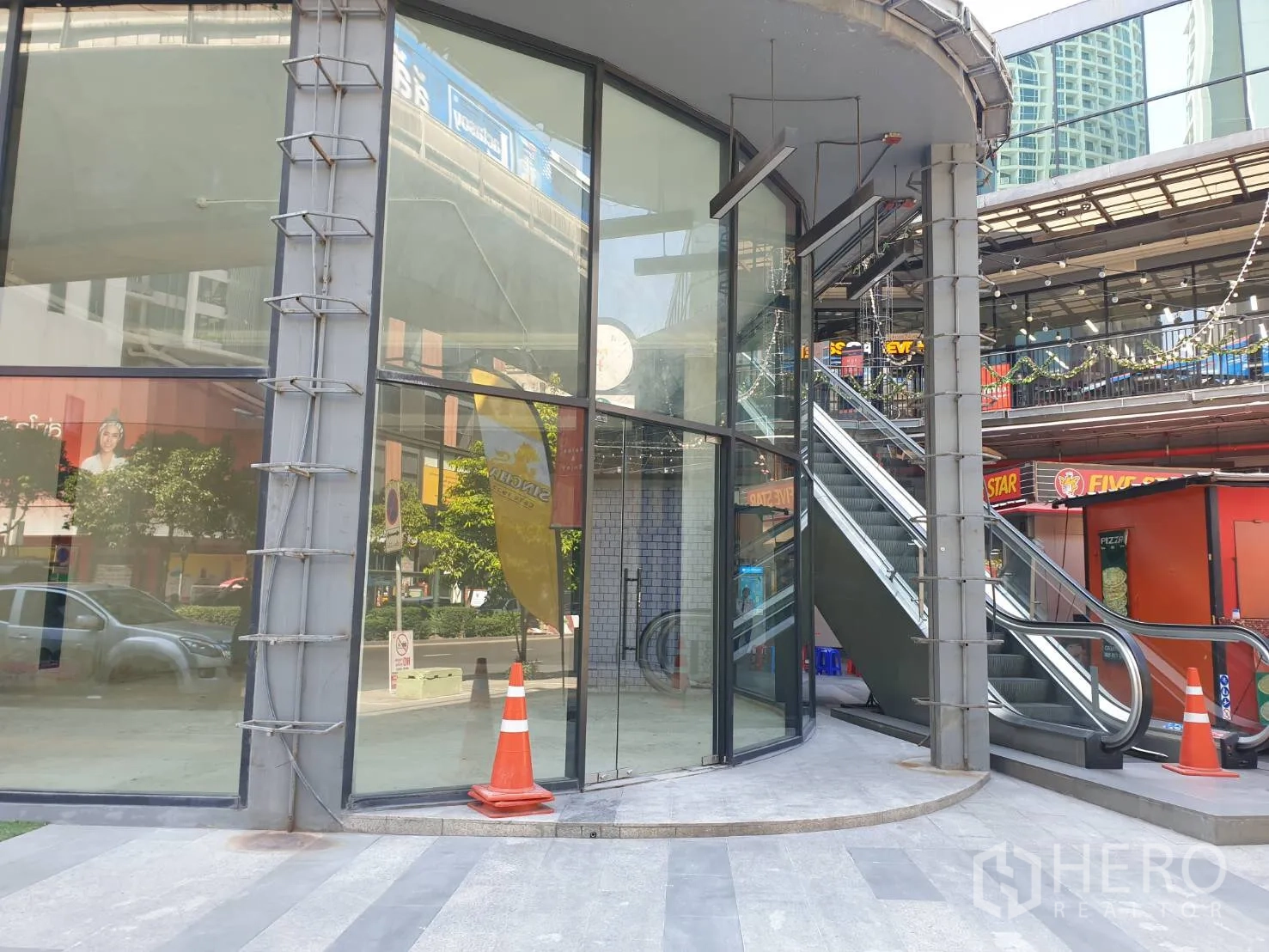 Retail Space for rent in Watthana, Bangkok - Corner retail storefront with curved full‑height glazing beside an outdoor escalator in a lifestyle complex.