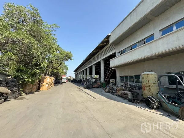 工厂 出租在Lat Lum Kaeo, Pathum Thani - 仓库侧通道，路旁有树木与堆放的材料