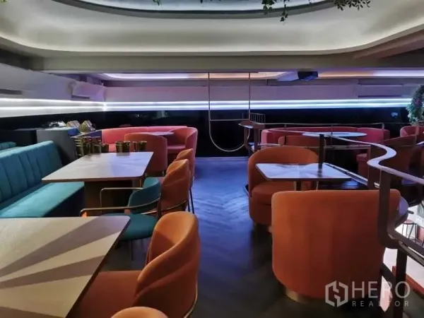 Retail Space for rent - Upper floor seating area with coral armchairs, square tables, and LED strip lighting.