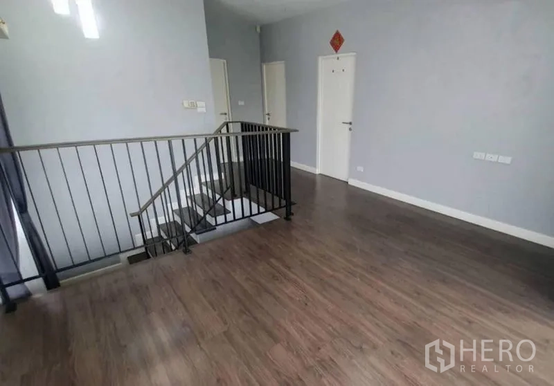 Detached House for sale in Pathum Thani - Bright upstairs landing with wood flooring and a black metal stair railing.