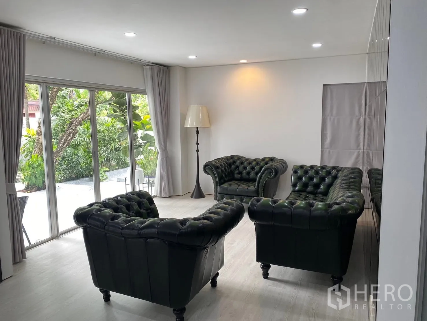 Detached House for rent in Suan Luang, Bangkok - Second living room with dark green Chesterfield sofas facing lush garden views.
