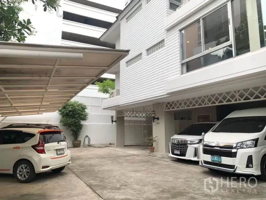 Townhouse for rent in Khlong Toei, Bangkok - Front courtyard of a white multi-storey townhouse with covered parking and cars.