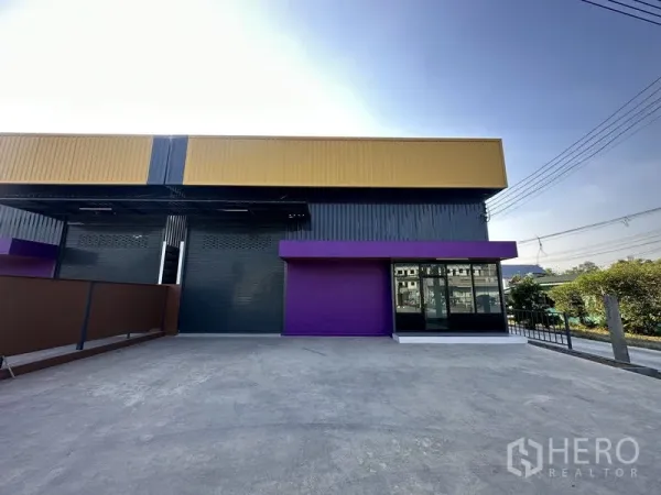 Warehouse for rent in Lam Luk Ka, Pathum Thani - Expansive concrete forecourt in front of the grey-and-yellow warehouse, ideal for truck loading.