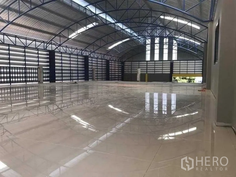 Warehouse for rent in Bang Pakong, Chachoengsao - Expansive warehouse floor with glossy tiles under a clear-span steel truss roof and roller shutters.