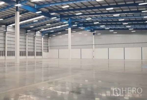 Warehouse for rent in Samut Prakan - Open-plan warehouse bay with white columns, reflective concrete floor, and metal insulated roof panels.