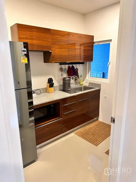 Detached House for sale in Prawet, Bangkok - Fitted kitchen with glossy wood cabinets, sink, window and appliances.