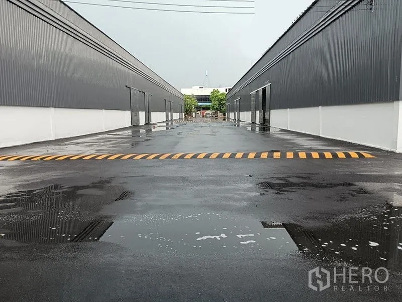 Warehouse for rent in Khlong Toei, Bangkok - Central driveway through the warehouse compound with reflective wet surface and a speed hump.