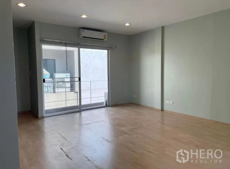 Townhouse for rent in Suan Luang, Bangkok - Open bedroom or family area with wood floors, recessed lighting and a sliding door to a small balcony.