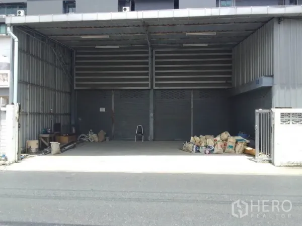 Warehouse for rent in Huai Khwang, Bangkok - Wide covered loading area with two large roller shutters and a concrete apron for truck access.
