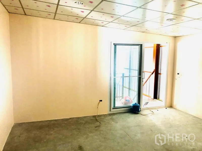 Warehouse for rent in Bang Kapi, Bangkok - Office area with a sliding glass door opening to a mezzanine, tiled ceiling, and unfinished floor.