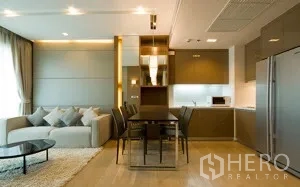 Condominium for rent in Khlong Toei, Bangkok - Open-plan living and dining area with sofa, glass-top table, and modern built-in kitchen in a Bangkok condo.