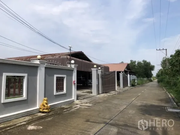 Detached House for sale in Lam Luk Ka, Pathum Thani - Gated entrance with high wall and sliding metal gate on a quiet road.