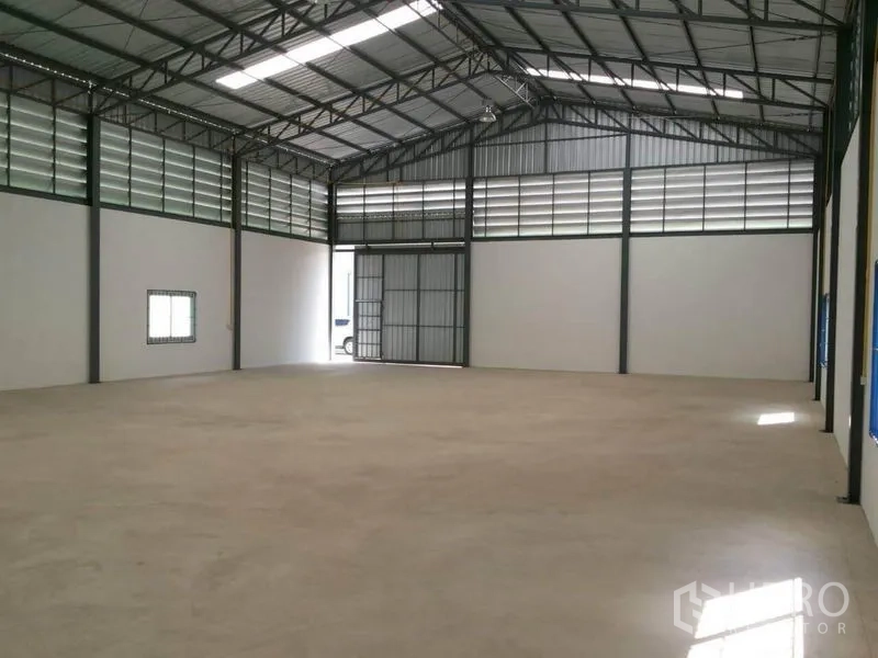Warehouse for rent in Lam Luk Ka, Pathum Thani - Spacious 375 sqm warehouse interior with high steel truss roof, louvered vents, and a large sliding entry door.