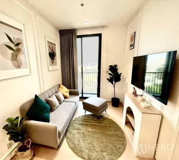 Condominium for sale - Bright living room with sofa, TV wall, balcony door and round rug in an Ekkamai condo.