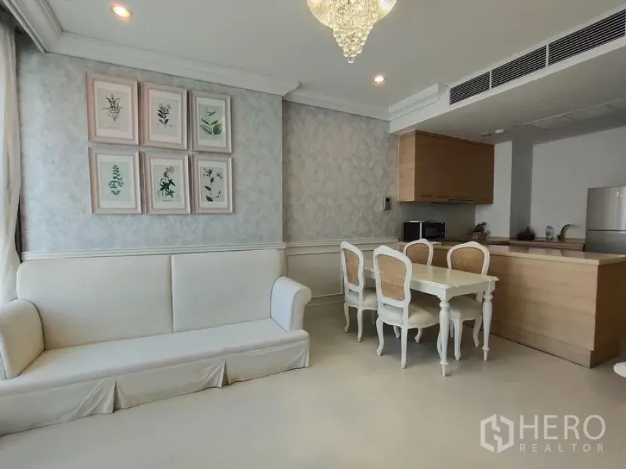 Condominium for rent in Khlong Toei, Bangkok - Open-plan living with sofa, white dining set and compact kitchen with wood cabinets and built-in appliances.