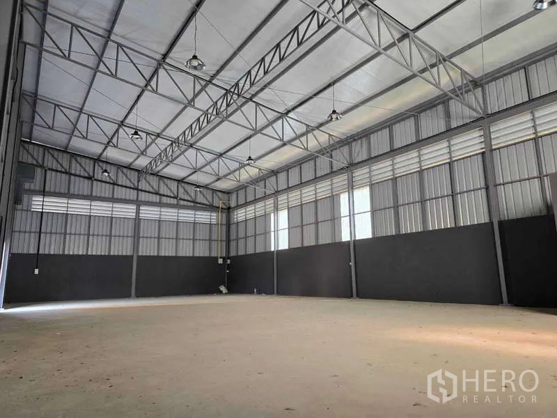Warehouse for rent in Mueang Samut Sakhon, Samut Sakhon - High‑clearance warehouse interior with metal trusses and hanging lights.
