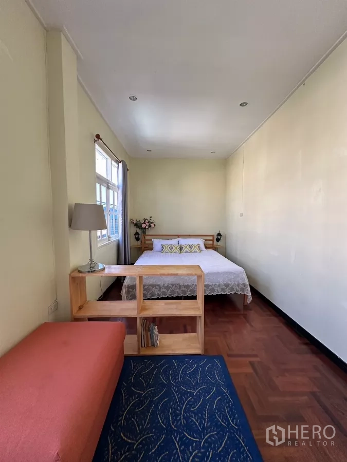 Home Office for rent in Suan Luang, Bangkok - Long bedroom with bed, sofa, and divider shelf by the window.