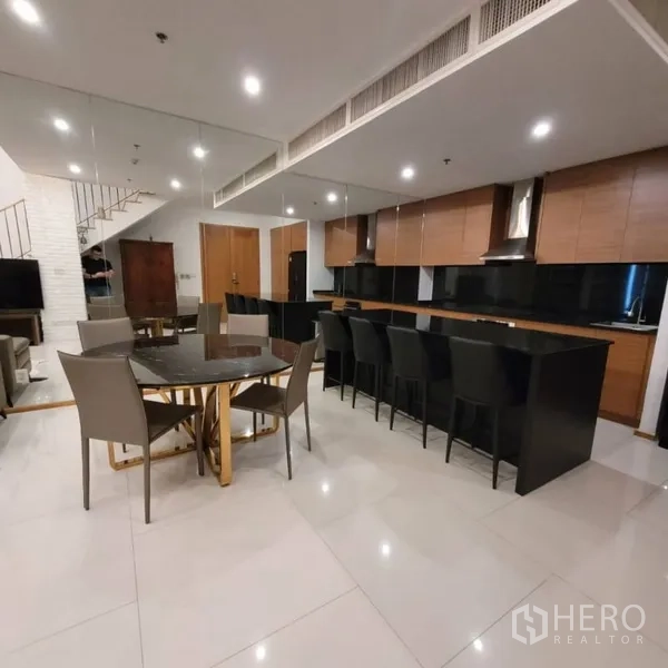 Condominium for rent in Khlong Toei, Bangkok - Spacious kitchen with long black island, bar stools, and adjacent dining table.