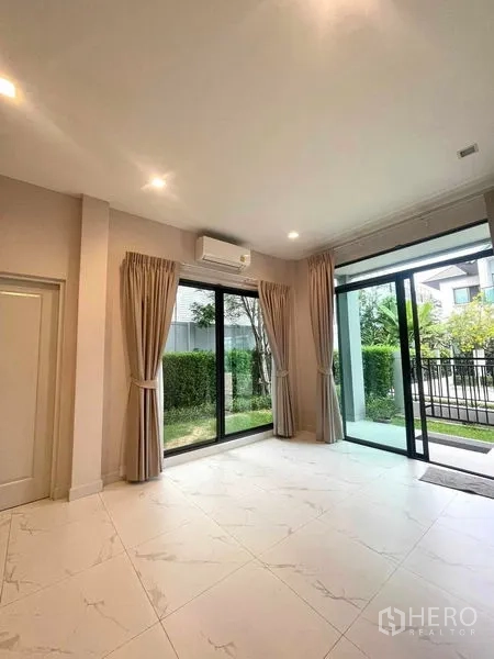 Detached House for sale in Bang Kruai, Nonthaburi - Living room angle showing twin sliding doors, sheer curtains and access to the front patio and lawn.
