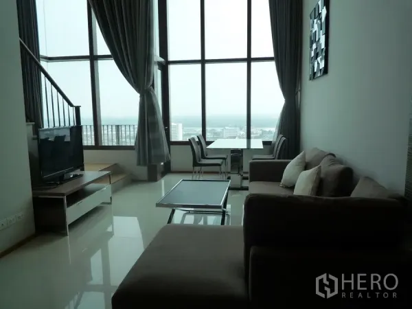 Condominium for rent in Khlong Toei, Bangkok - Double-height living area with floor-to-ceiling windows, dining set and city view.