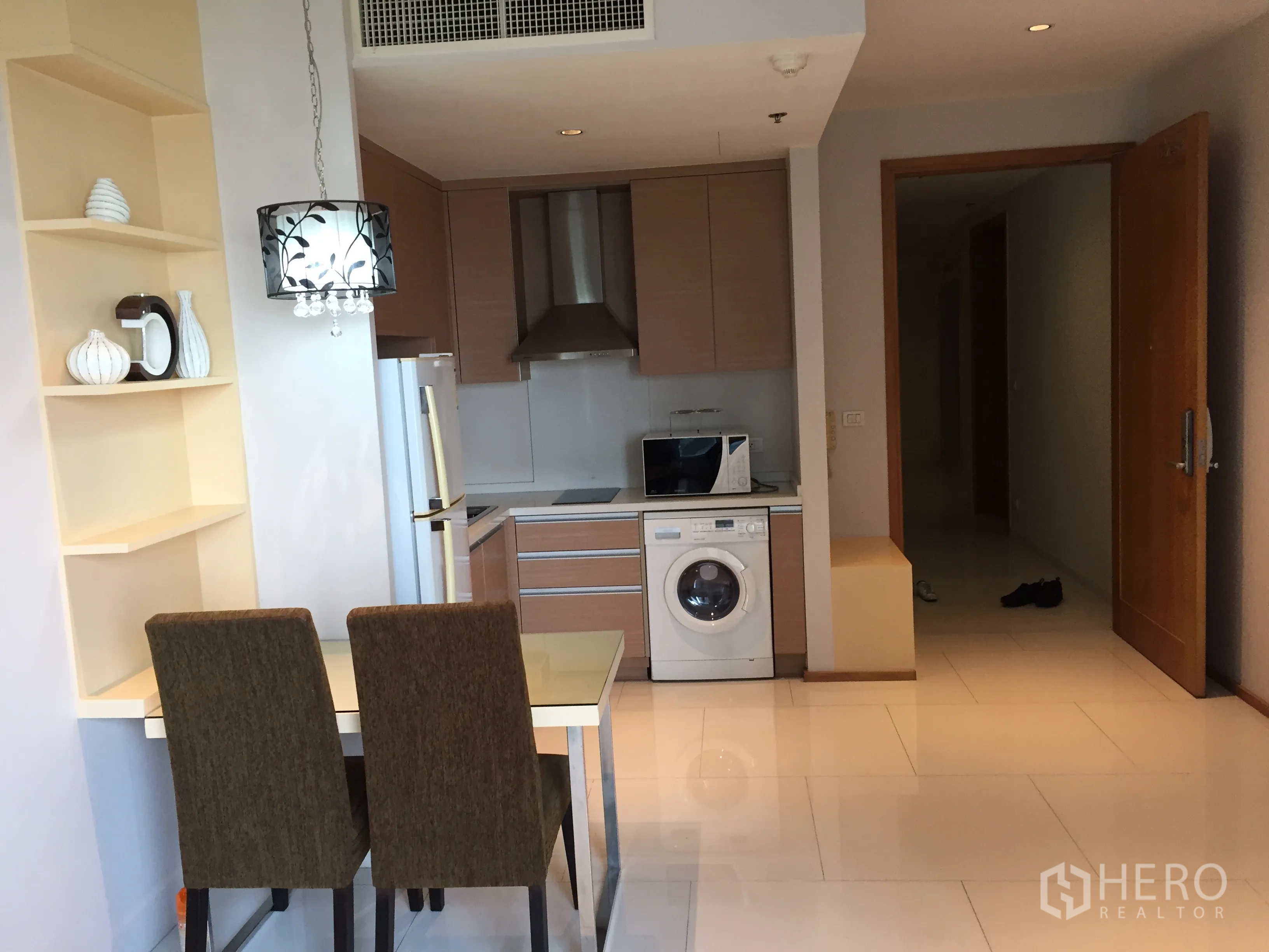 Condominium for rent or sale in Khlong Toei, Bangkok - Open-plan kitchenette with two-seat dining table, shelving and entry hallway in a contemporary apartment.