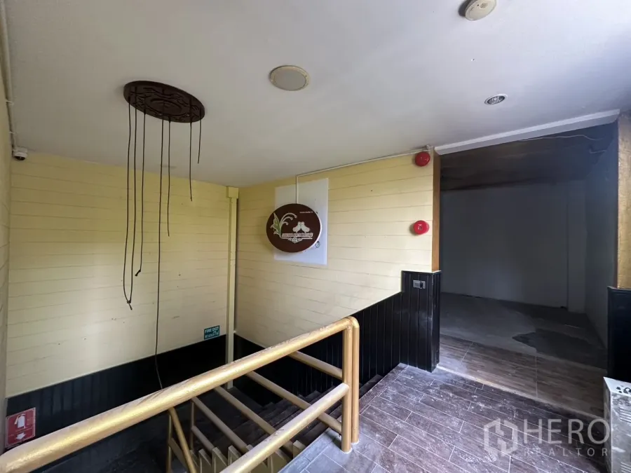 Retail Space for rent in Bang Rak, Bangkok - Stair landing leading to a bare‑shell retail floor with wooden handrail and safety fixtures.
