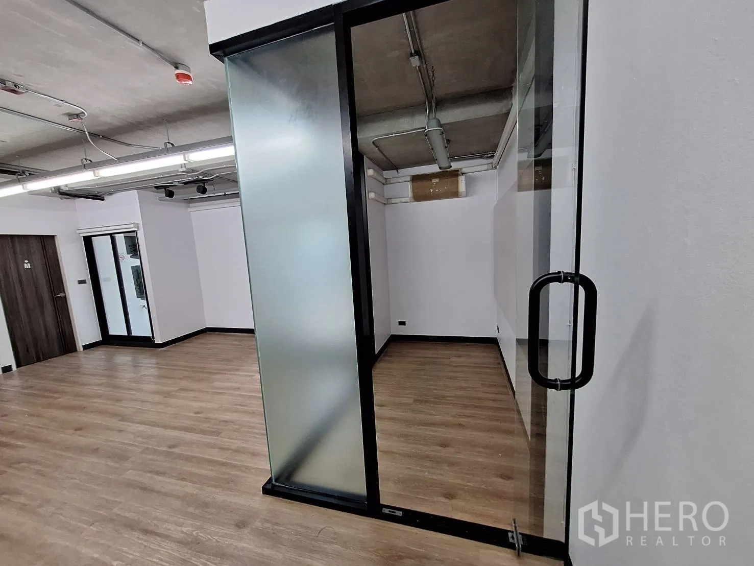 Office Space for rent - Glass door corridor leading to a bright office with wood floors.