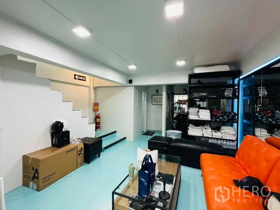 Shophouse for sale in Watthana, Bangkok - Lounge and storage area with orange sofa, shelving, and internal staircase.