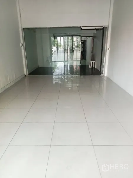 店屋 出租在Phra Khanong, Bangkok - 一层明亮营业空间，白色亮面地砖、挑高天花与玻璃隔断通向推拉门。