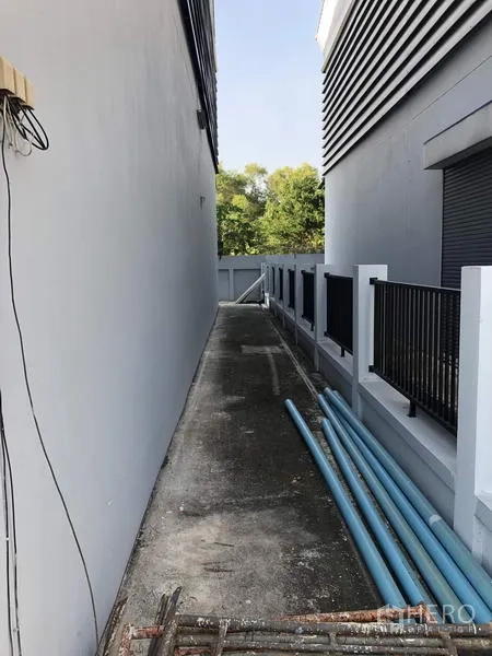 Factory for rent in Lam Luk Ka, Pathum Thani - Narrow service walkway with drainage and visible PVC pipes along the boundary fence.