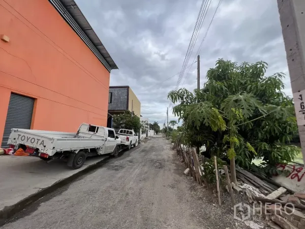 Warehouse for rent or sale in Lat Krabang, Bangkok - Gravel road in front of the warehouse with utility poles and trees, suitable for truck approach.