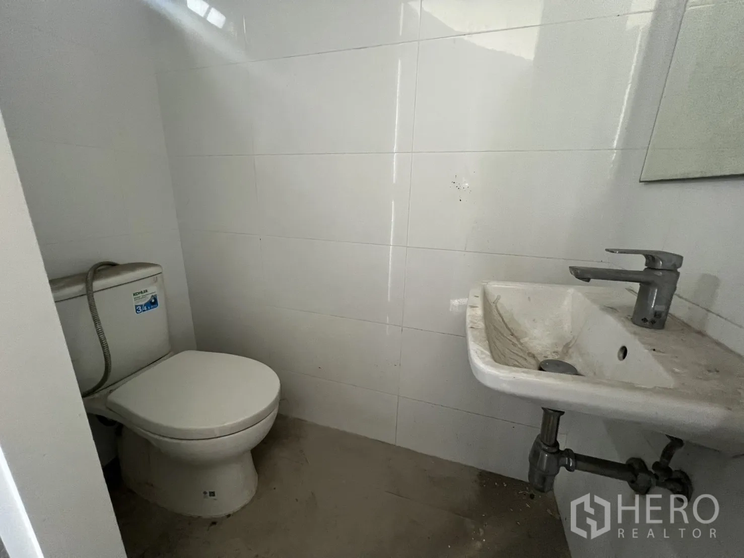Retail Space for rent - Basic restroom with toilet and wall-mounted sink in a white-tiled room.