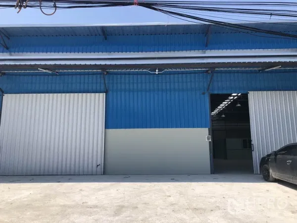 Warehouse for rent in Khlong Luang, Pathum Thani - Blue metal-clad warehouse facade with wide sliding doors and a concrete loading apron in Khlong Luang.