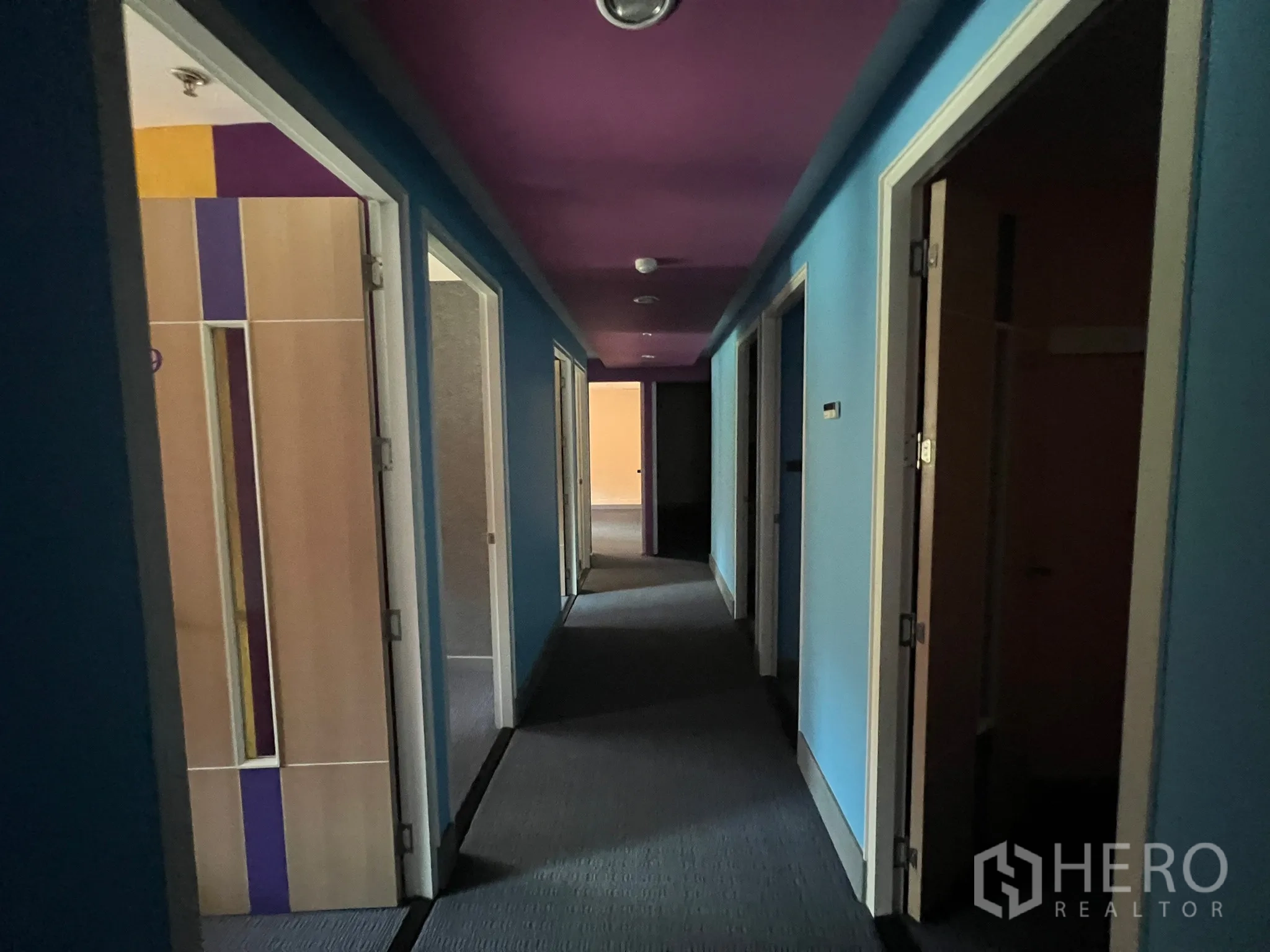 Retail Space for rent - Hallway with multiple partitioned rooms, blue walls and a purple ceiling leading to the back area.