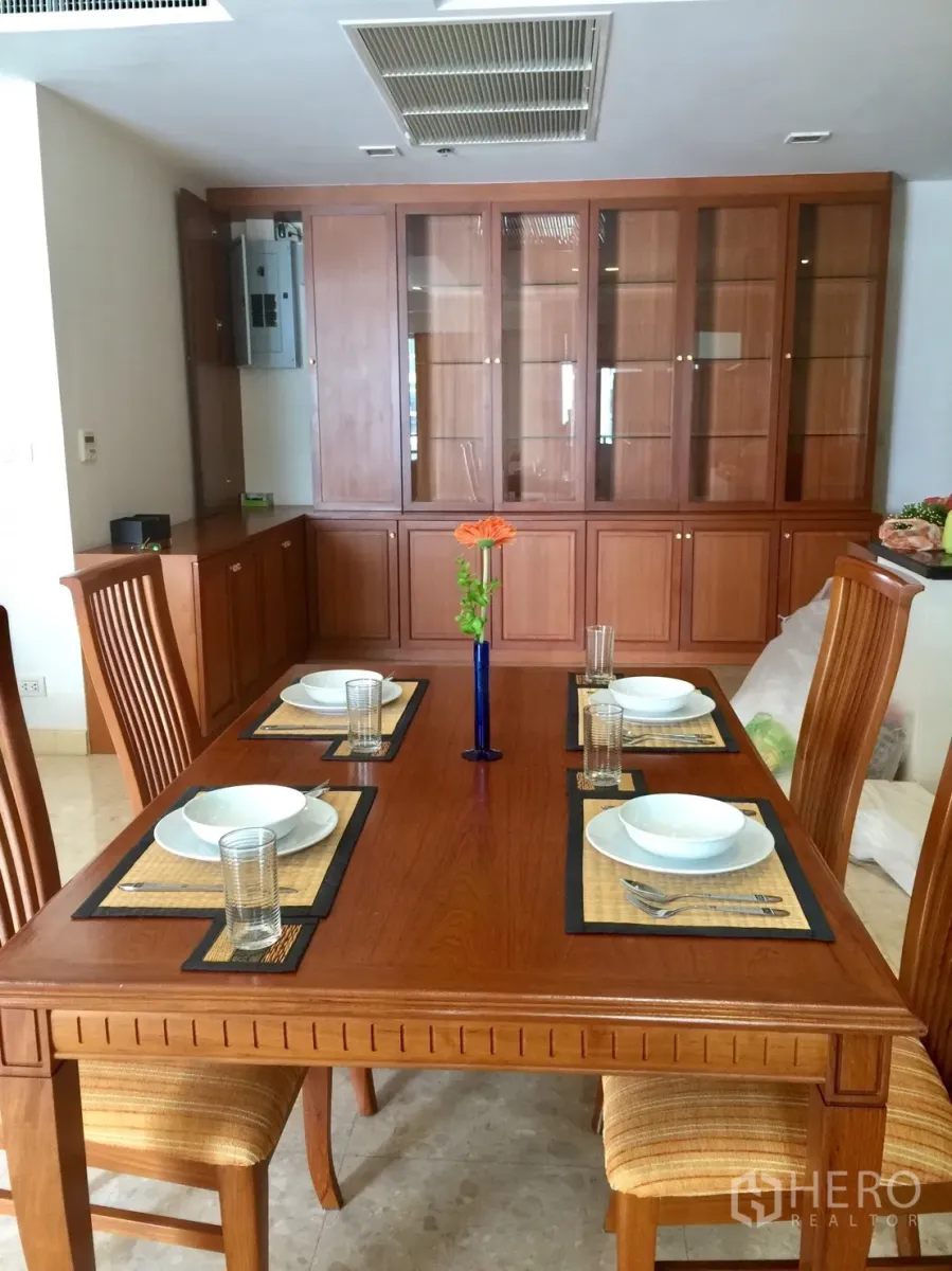 Condominium for rent in Khlong Toei, Bangkok - Dining area with solid wood table set for four and built-in glass cabinetry.