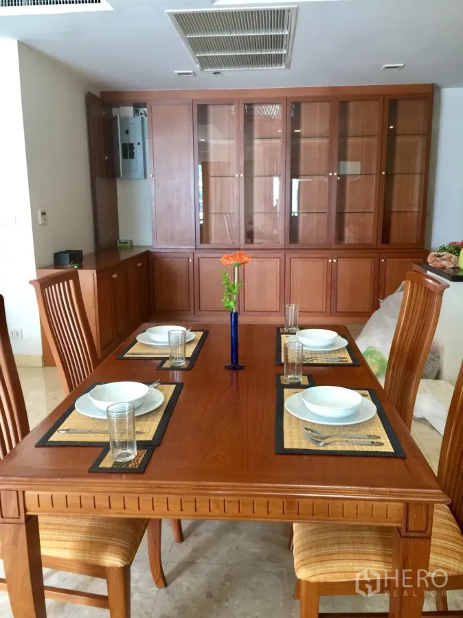Condominium for rent in Khlong Toei, Bangkok - Dining area with solid wood table set for four and built-in glass cabinetry.