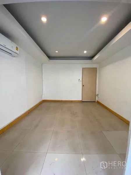 Townhouse for rent in Khlong Toei, Bangkok - Bright empty room with recessed lighting, tiled floor, and wall-mounted air conditioner.