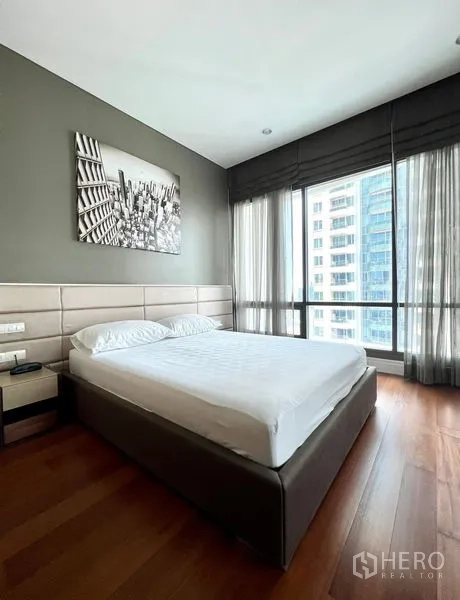 Condominium for rent in Khlong Toei, Bangkok - Bright bedroom with city views through corner windows and an upholstered headboard.