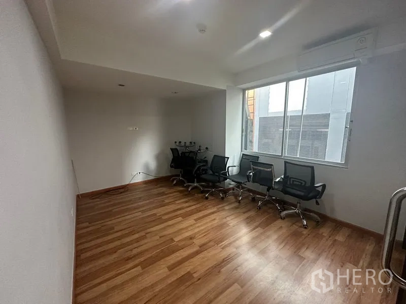 Office Space for rent in Khlong Toei, Bangkok - Bright office room with a large window, wood laminate floor, a row of chairs, and a wall-mounted air conditioner.