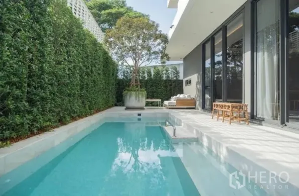 Detached House for sale in Suan Luang, Bangkok - Private outdoor swimming pool bordered by tall hedges with seating along the terrace and sliding glass doors.