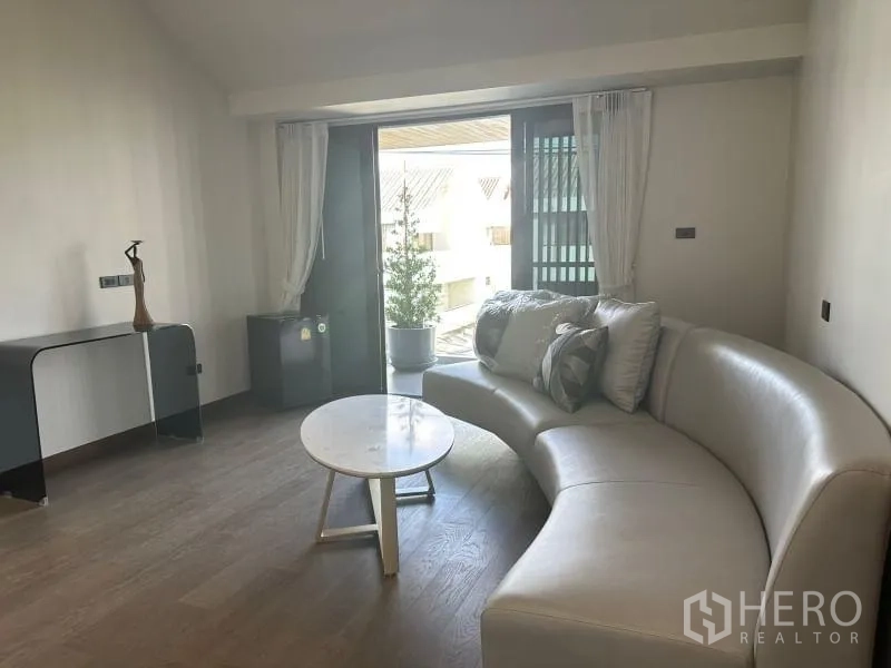 独立式住宅 出租在Suan Luang, Bangkok - 楼上休闲区，弧形沙发、茶几与阳台玻璃门。