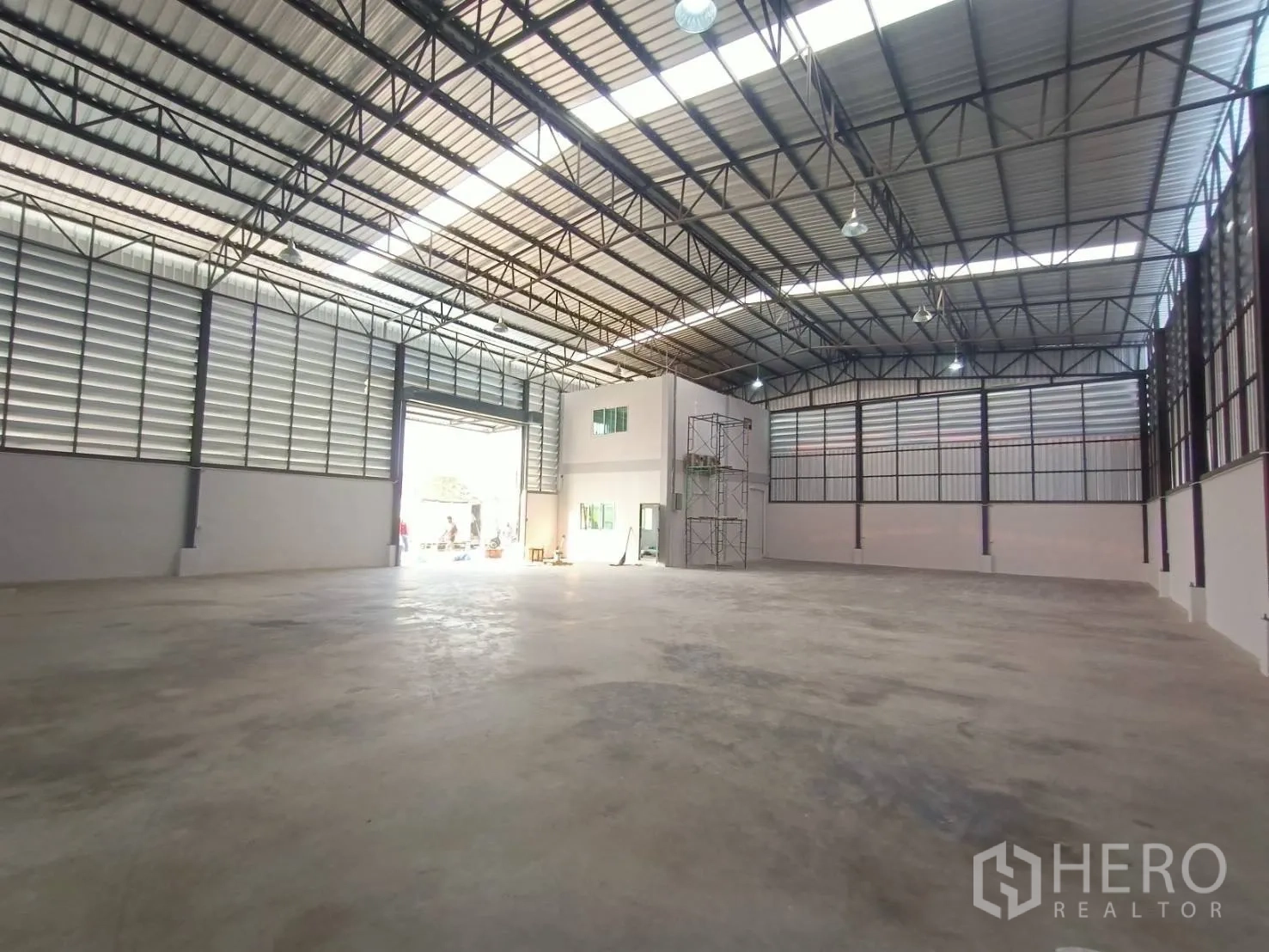 Factory for rent or sale in Mueang Samut Sakhon, Samut Sakhon - Open production space with skylight strips, large roller shutter door, and attached office block inside the warehouse.